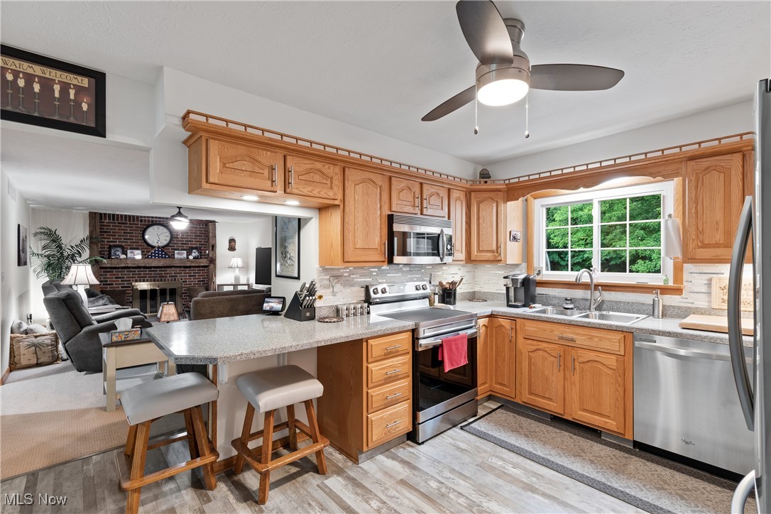 4640 Sherman Road Kent, OH 44240 - Photo 12 of 37 Kitchen with appliances with stainless steel finishes, a ceiling fan, backsplash, a peninsula, and a brick fireplace
