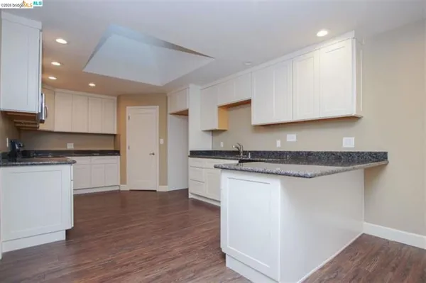a kitchen with stainless steel appliances granite countertop a sink stove and white cabinets with wooden floor