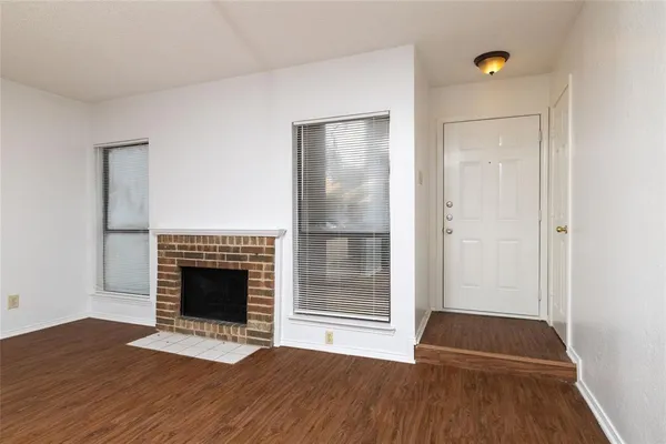 a view of an empty room with wooden floor fireplace and a window
