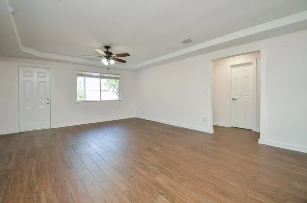 an empty room with wooden floor chandelier fan and windows