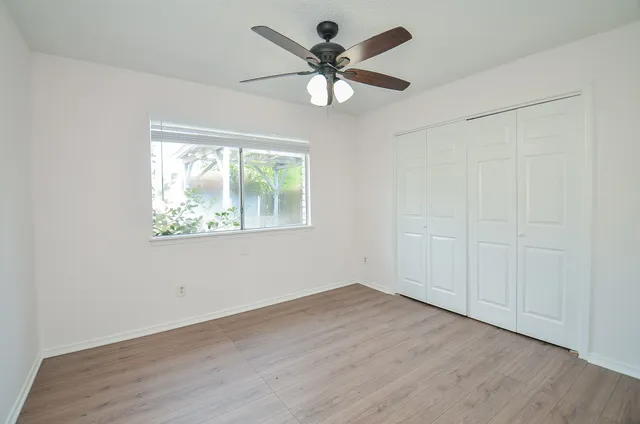an empty room with wooden floor chandelier fan and windows