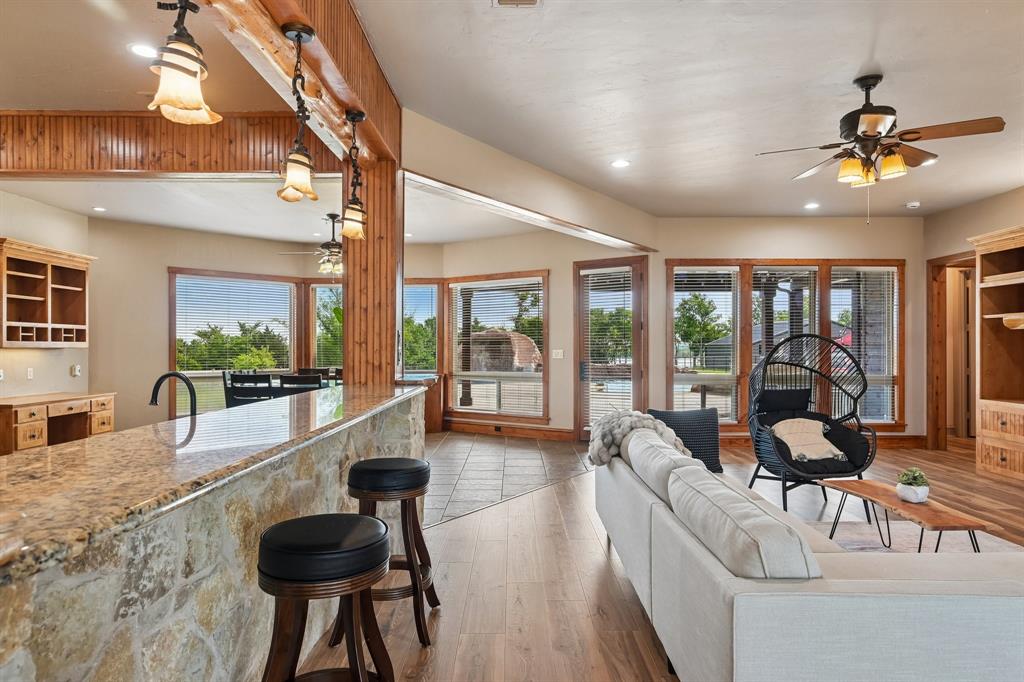 2085 Switzer Road Sanger, TX 76266 - Photo 7 of 39 Open-concept living space featuring wood-finish flooring, a stone-clad breakfast bar with a granite countertop, and extensive window-framed exterior views