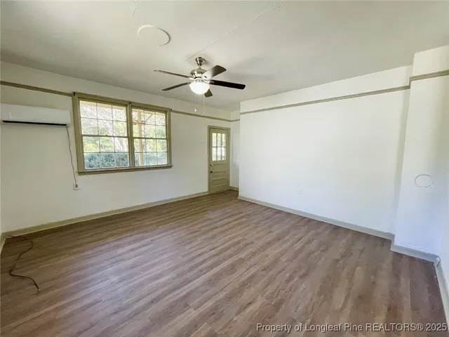 an empty room with wooden floor chandelier fan and windows