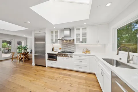 a kitchen with stainless steel appliances a stove a sink a refrigerator white cabinets and wooden floor