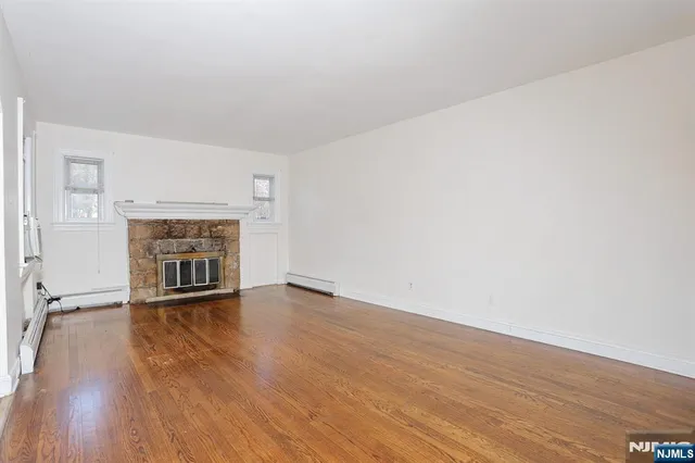 a view of an empty room with wooden floor fireplace and a window