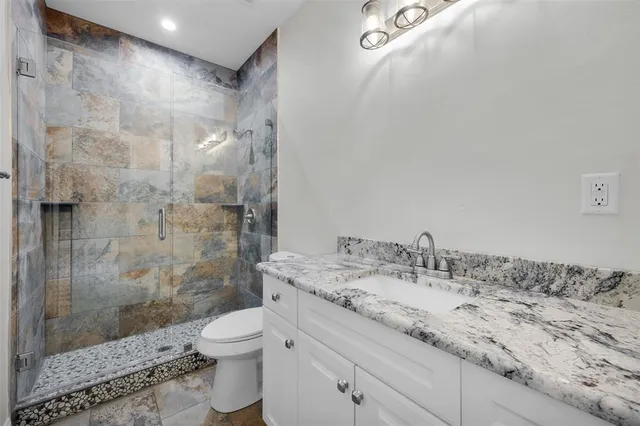 a bathroom with a granite countertop sink a toilet and shower
