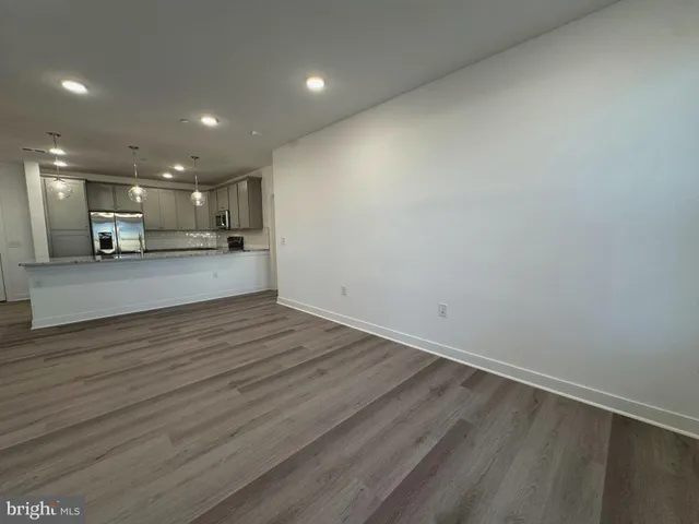 an empty room with wooden floor kitchen view and a window