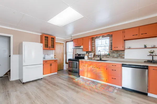 a kitchen with stainless steel appliances granite countertop a refrigerator a sink dishwasher a stove and white countertops with wooden floor
