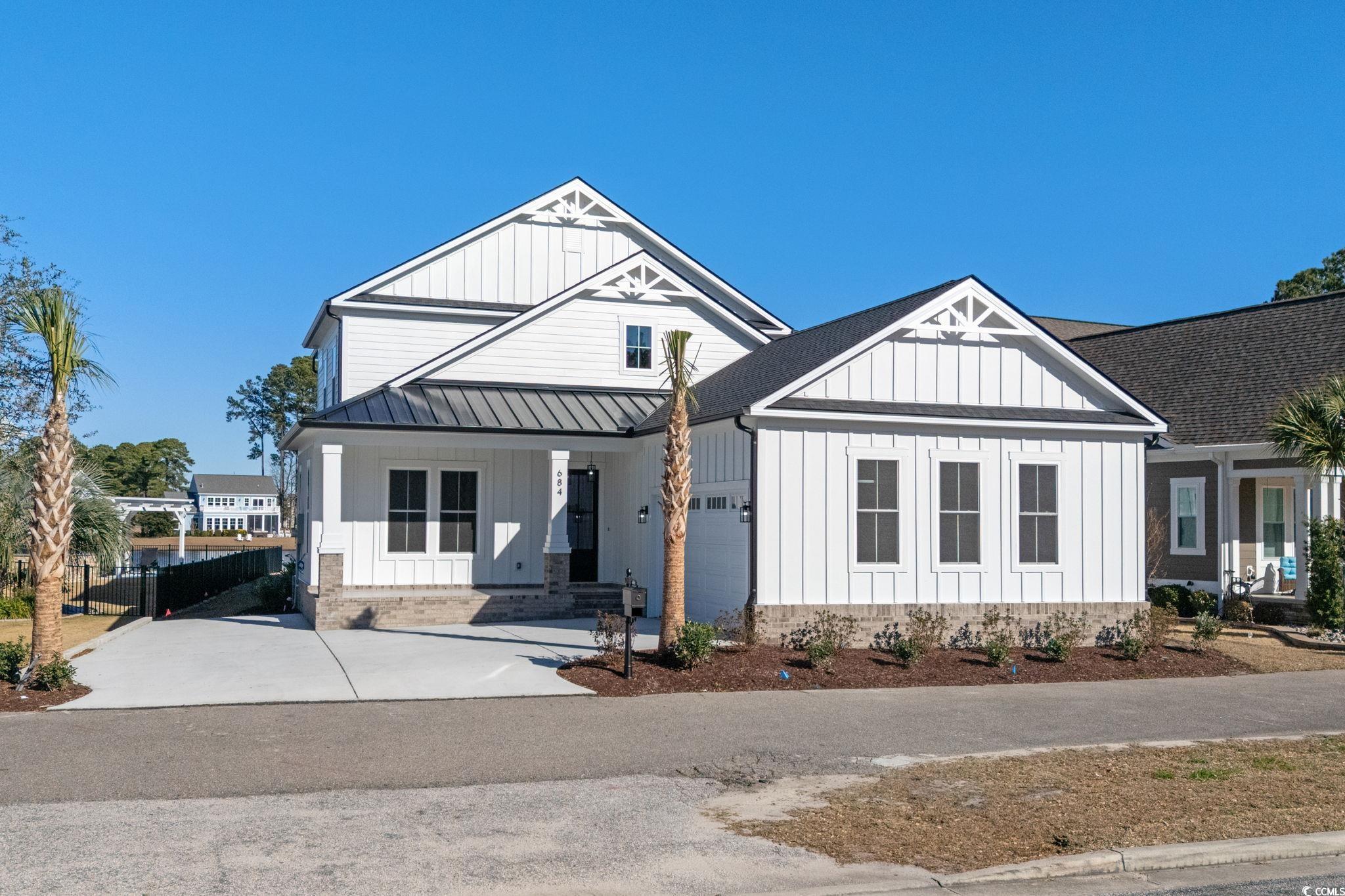 Modern farmhouse featuring board and batten siding, a porch, driveway, and a standing seam roof