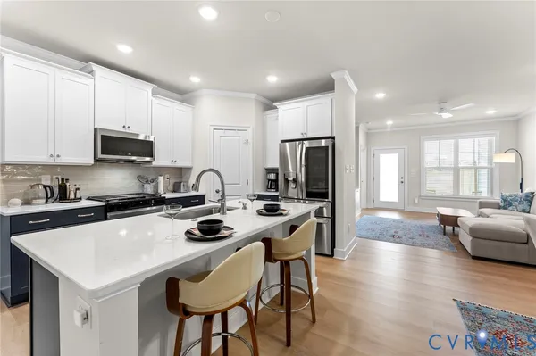 a kitchen with stainless steel appliances granite countertop a stove a refrigerator a sink a stove and white cabinets with wooden floor