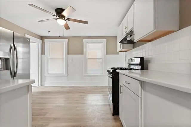 a view of a kitchen with a sink stainless steel appliances wooden floor and a window