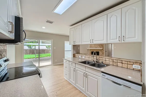 a kitchen with granite countertop a sink a stove top oven a counter space and cabinets