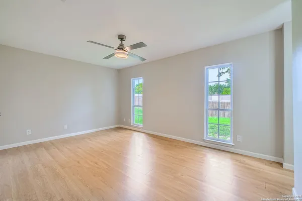 an empty room with wooden floor ceiling fan and windows