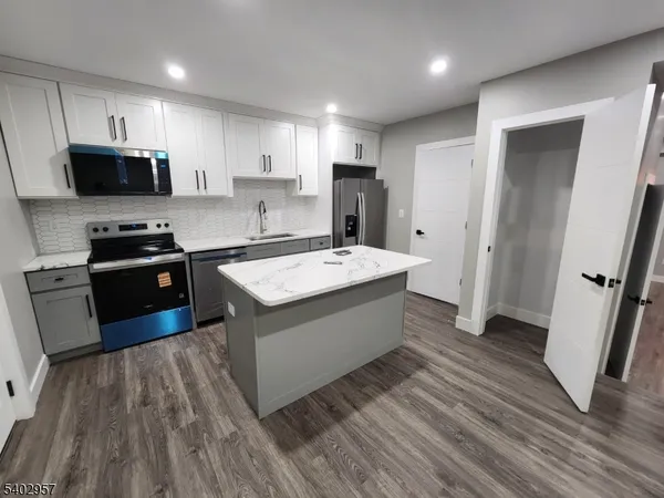 a kitchen with stainless steel appliances a sink dishwasher a refrigerator a stove top oven a wooden floor and cabinets