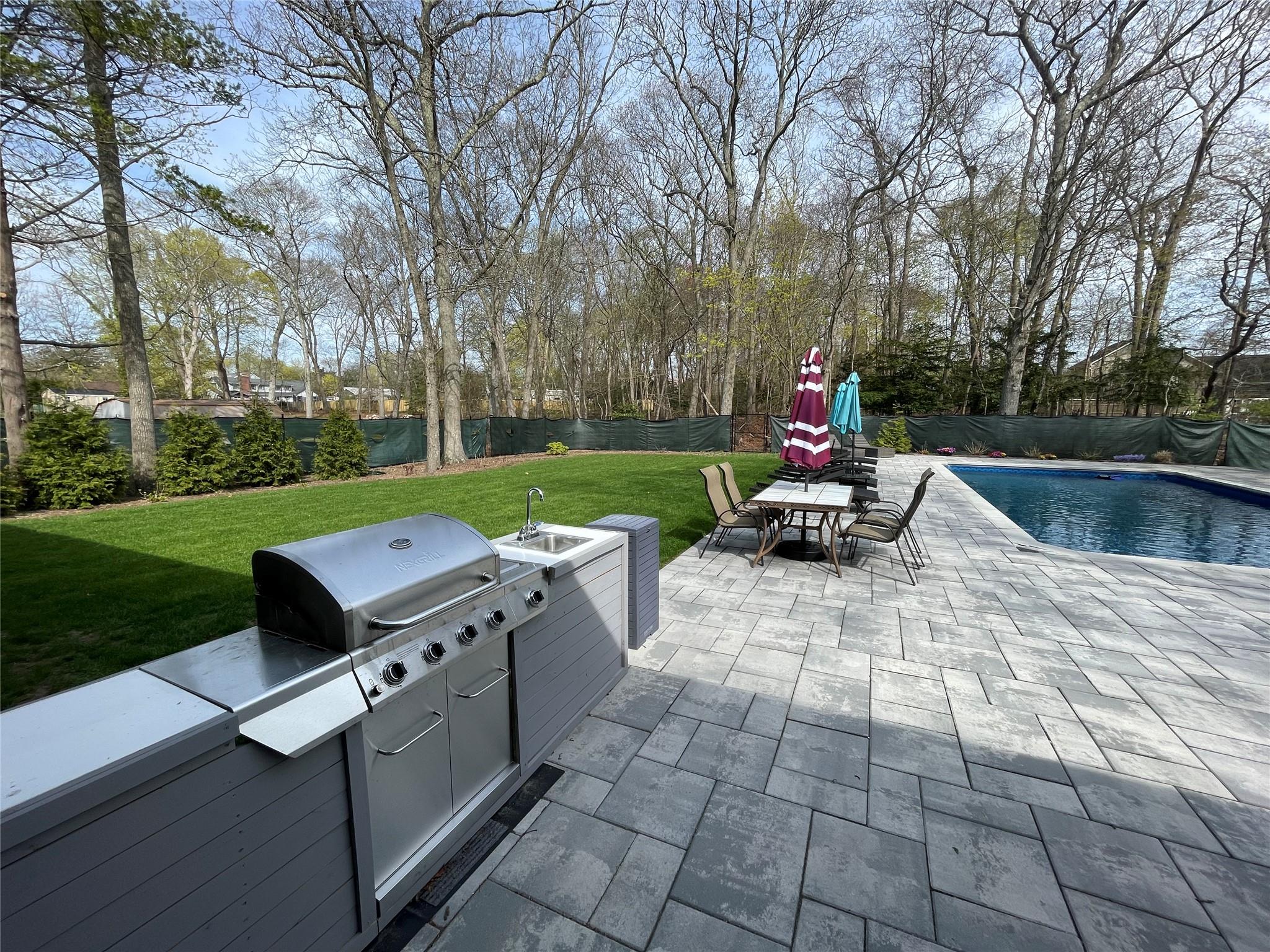 47 Beachfern Road Center Moriches, NY 11934 - Photo 1 of 1 View of patio / terrace featuring a fenced in pool, exterior kitchen, outdoor dining space, a sink, and a fenced backyard