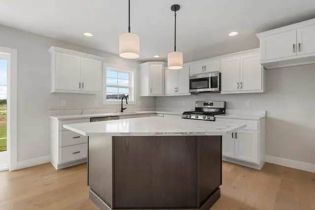 a kitchen with stainless steel appliances granite countertop a sink a stove a refrigerator and white cabinets