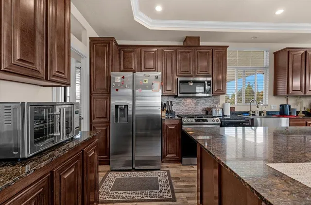a kitchen with stainless steel appliances granite countertop a refrigerator a stove and a sink with wooden cabinets