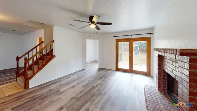 a view of an empty room with wooden floor fireplace and a window