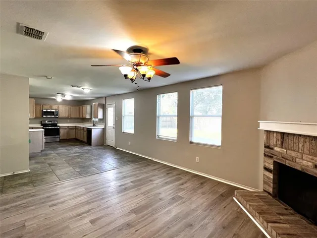 a view of an empty room and kitchen with wooden floor