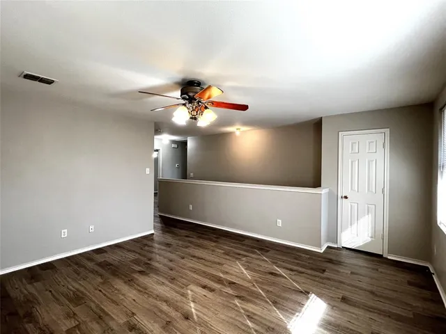 a view of an empty room with wooden floor and chandelier fan