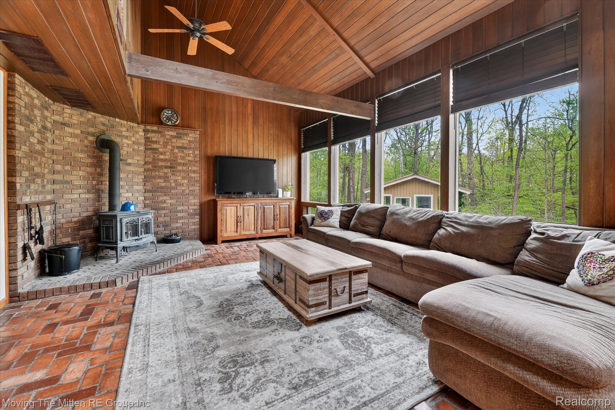 Living area with brick floors, a ceiling fan, a wood stove, a high wood beamed ceiling, and wooden walls