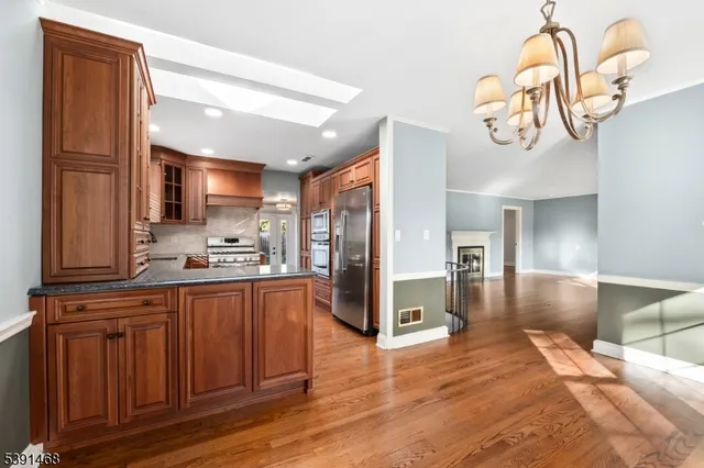 a kitchen with stainless steel appliances granite countertop a refrigerator a sink dishwasher and wooden cabinets with wooden floor