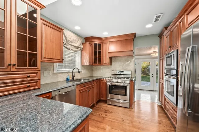 a kitchen with stainless steel appliances granite countertop a stove a sink dishwasher a refrigerator and cabinets with wooden floor