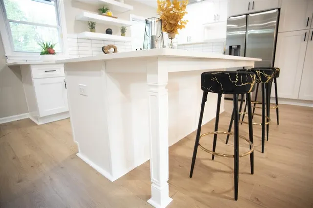 a kitchen with stainless steel appliances kitchen island granite countertop a stove a sink a refrigerator and white cabinets with wooden floor