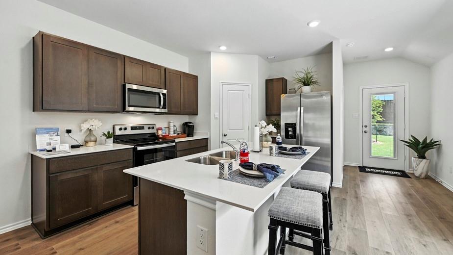 646 Glee Stem Road Lavon, TX 75166 - Photo 8 of 17 Modern kitchen featuring dark wood-finish cabinetry, white solid surface countertops, stainless steel appliances, and wood-finish flooring