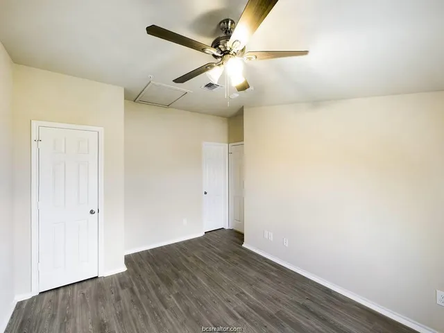 an empty room with wooden floor fan and windows