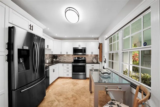 a kitchen with stainless steel appliances granite countertop a refrigerator a stove and a sink with large window