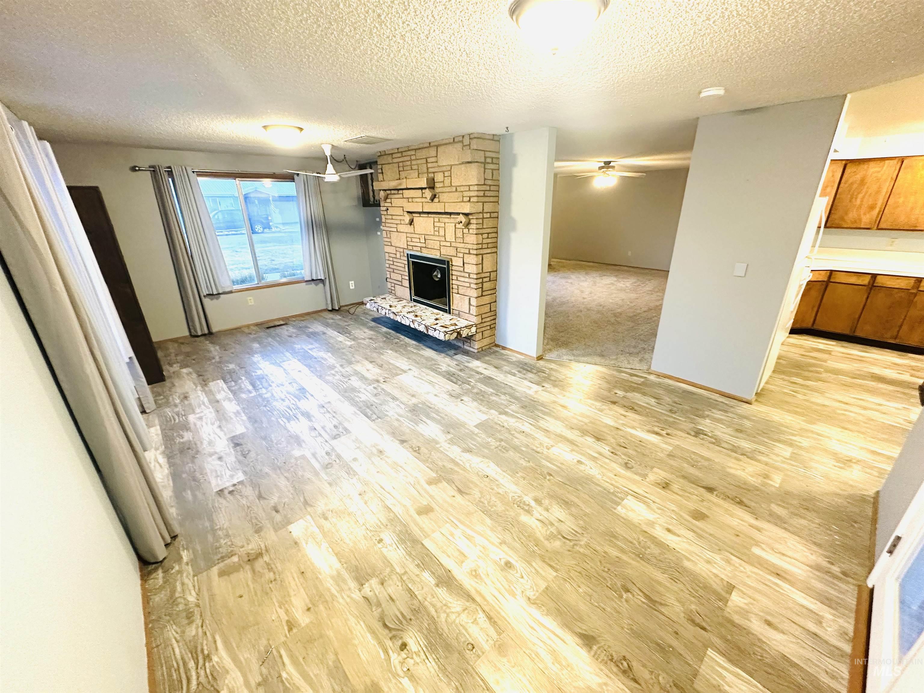 1111 West D Street Vale, OR 97918 - Photo 9 of 26 Unfurnished living room with a fireplace, light wood-style flooring, and a textured ceiling