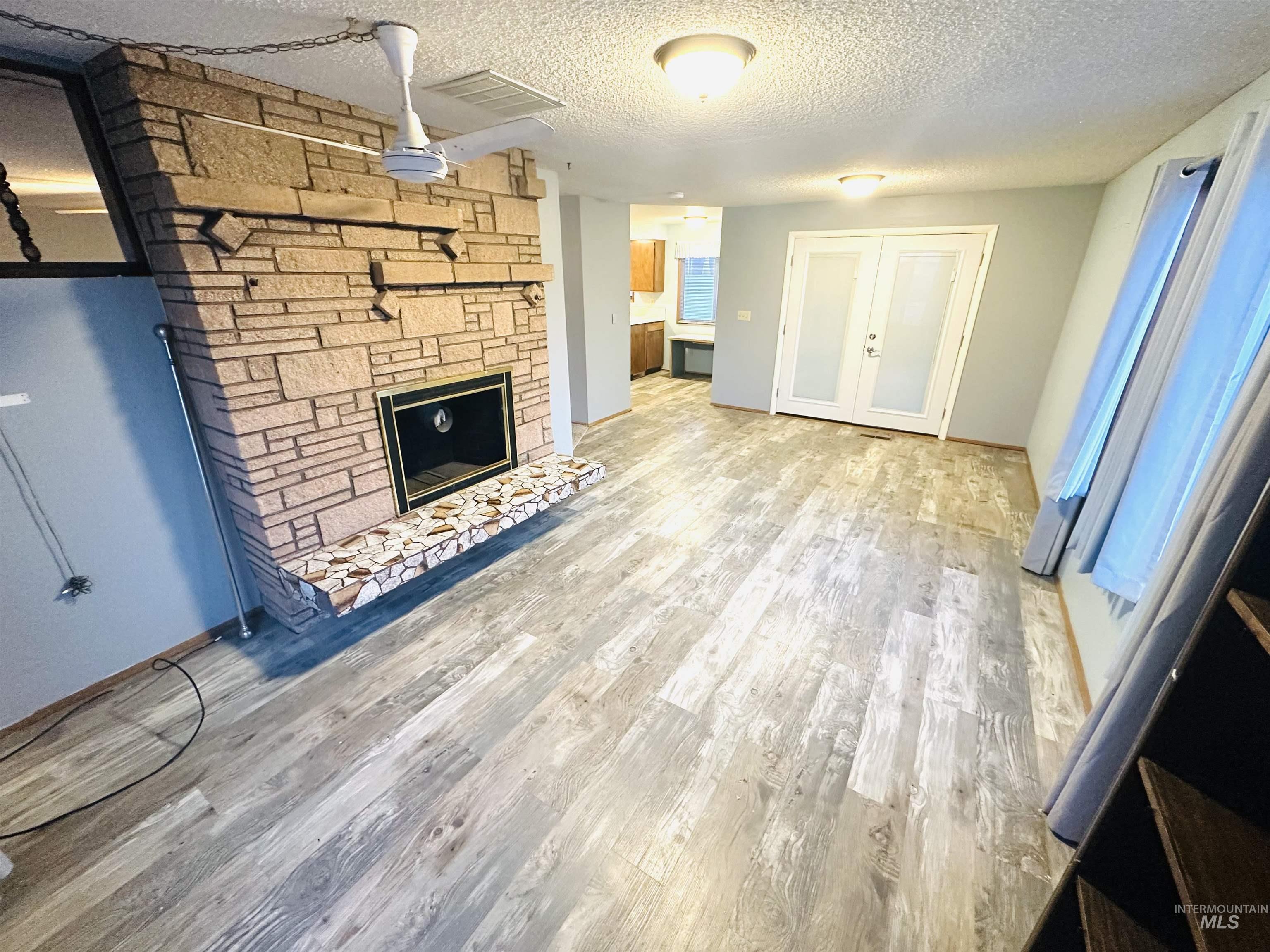 1111 West D Street Vale, OR 97918 - Photo 10 of 26 Unfurnished living room featuring a textured ceiling, light wood-type flooring, and a fireplace