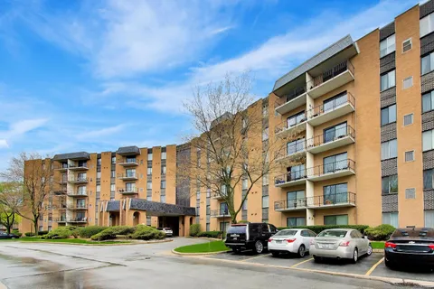 a front view of a building with lot of cars and trees