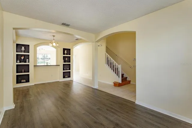 a view of an empty room with wooden floor and kitchen view