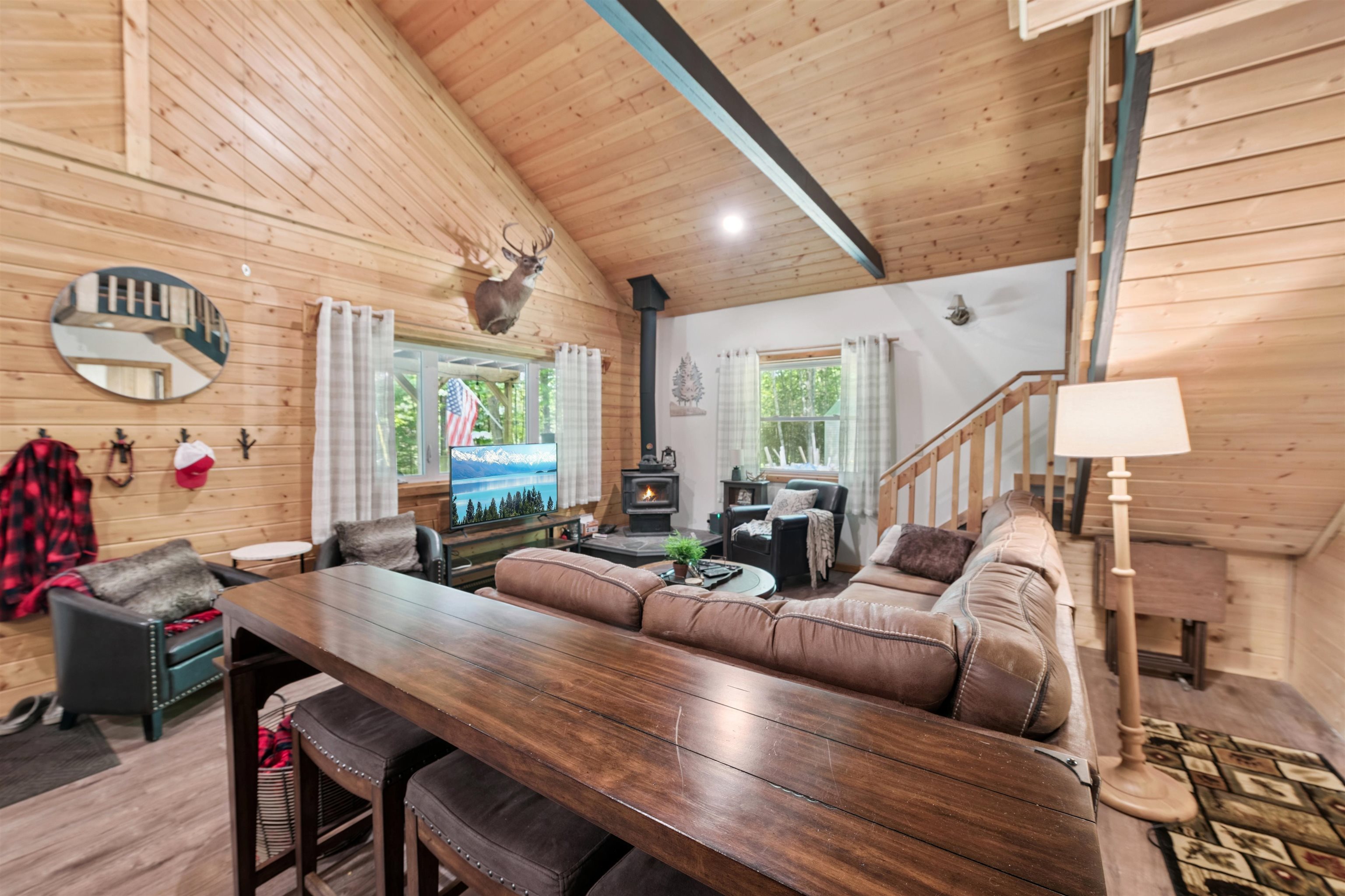 Living room with a wood stove, stairs, light wood-style floors, wood walls, and a wooden ceiling with exposed beams