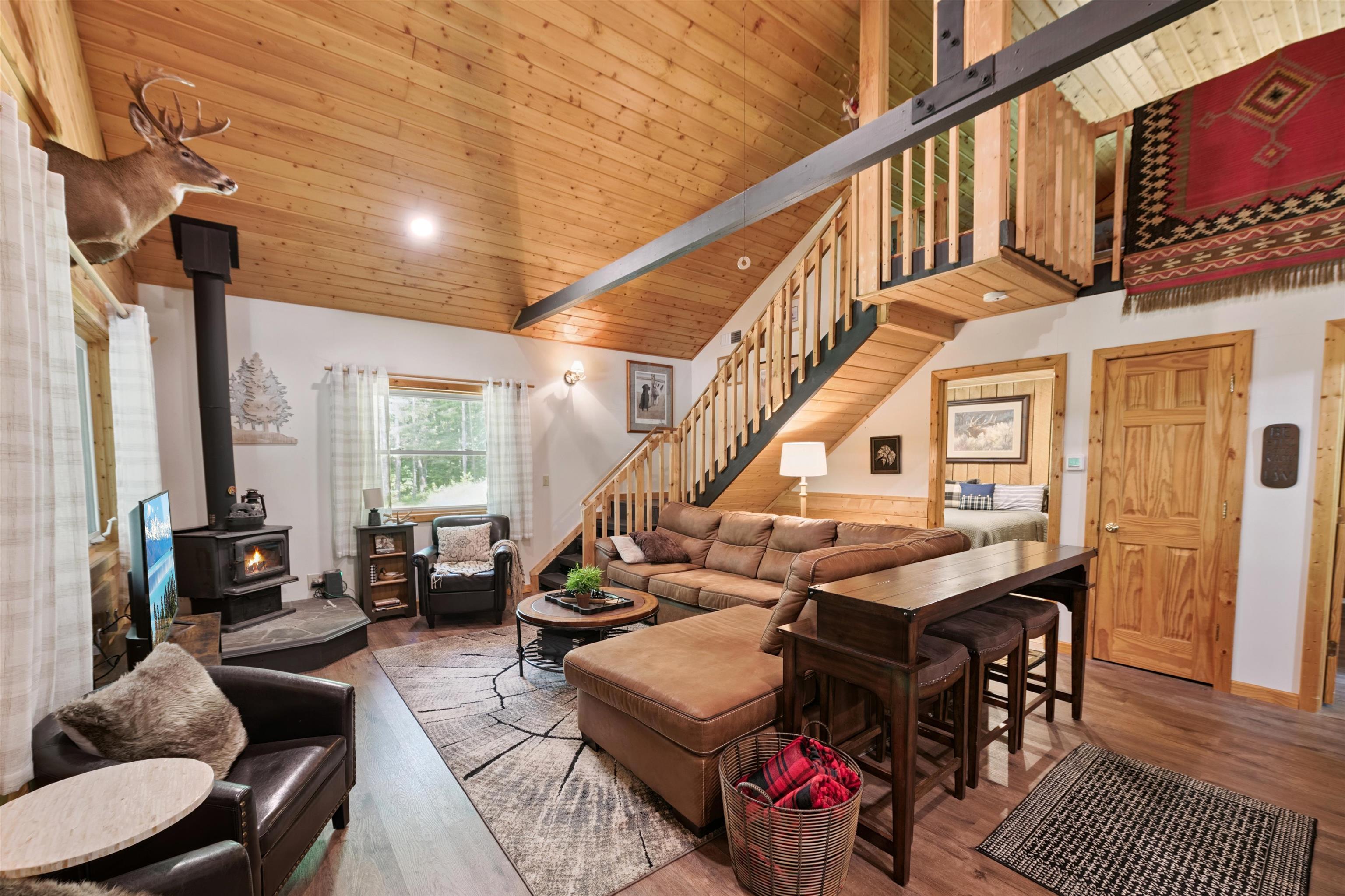 Living room with a wood stove, stairs, wood finished floors, high vaulted ceiling, and wood ceiling