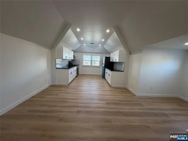 an empty room with wooden floor and kitchen view