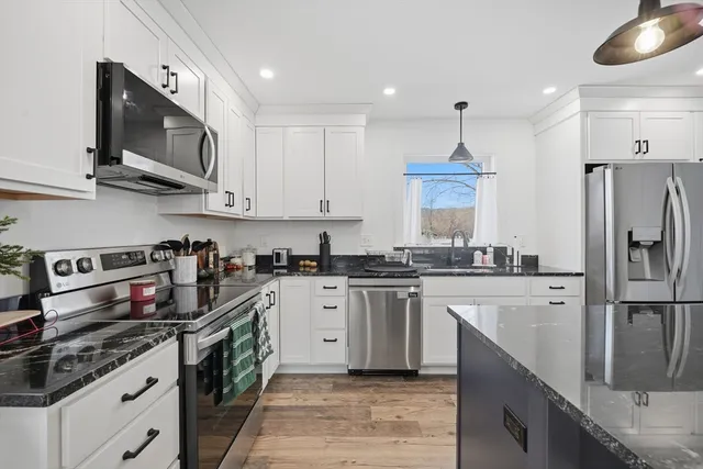 a kitchen with stainless steel appliances granite countertop a stove top oven a sink dishwasher and a refrigerator with wooden cabinets