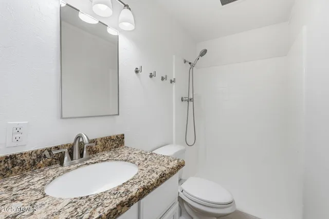 a bathroom with a granite countertop sink toilet a mirror and shower