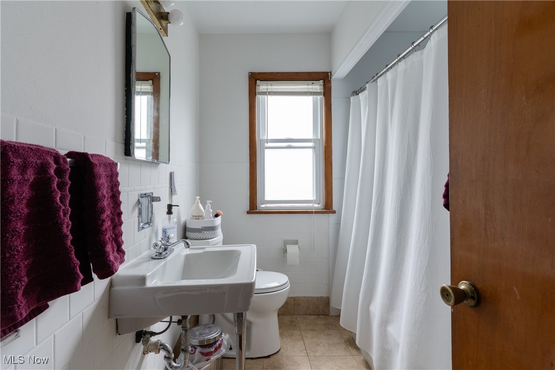 14220 Triskett Road Cleveland, OH 44111 - Photo 17 of 32 Bathroom featuring tile walls, toilet, tile patterned flooring, a wainscoted wall, and a shower with curtain