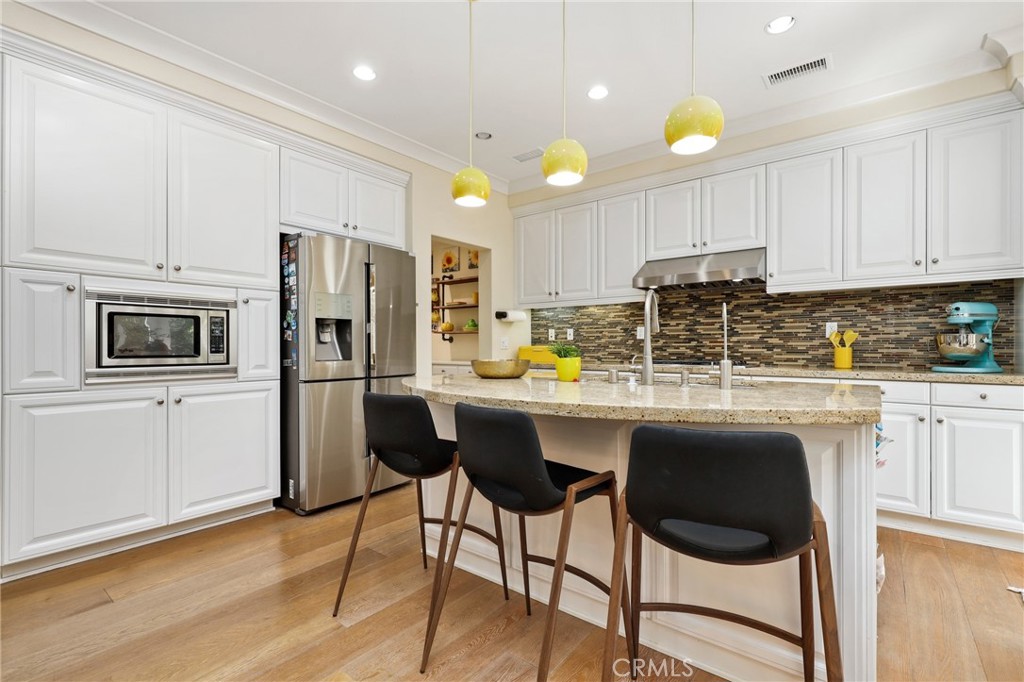 24 Lacebark, Unit 48 Irvine, CA 92618 - Photo 9 of 42 a kitchen with stainless steel appliances granite countertop a stove a sink a microwave a refrigerator and white cabinets with wooden floors