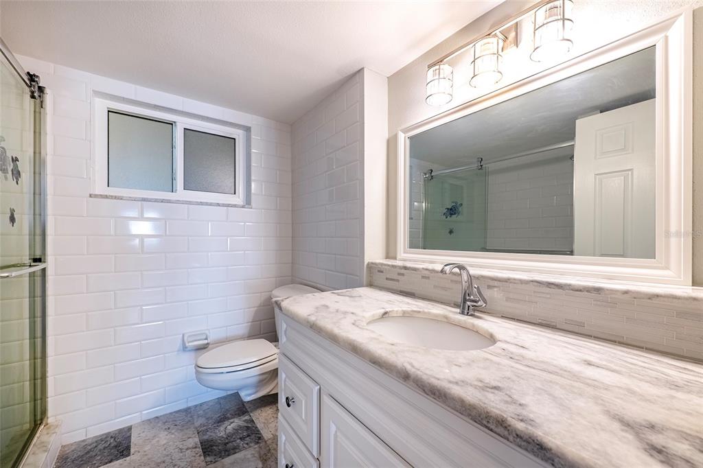 620 Edgewater Drive, Unit 103 Dunedin, FL 34698 - Photo 10 of 26 a bathroom with a granite countertop sink a toilet and a mirror