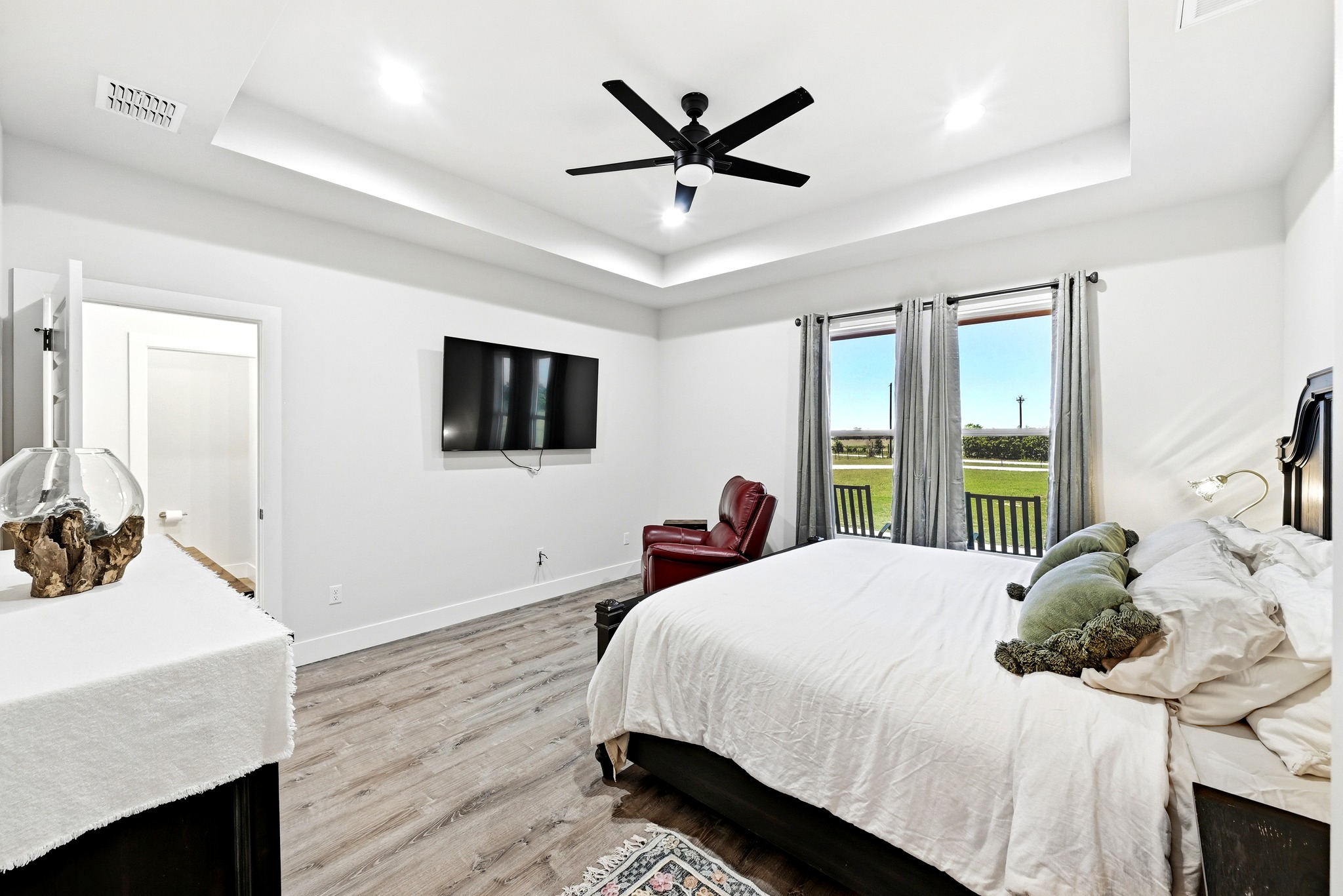 2889 Old McMahan Road Lockhart, TX 78644 - Photo 18 of 33 Recessed lighting illuminates this inviting primary bedroom, featuring a tray ceiling and wood flooring.