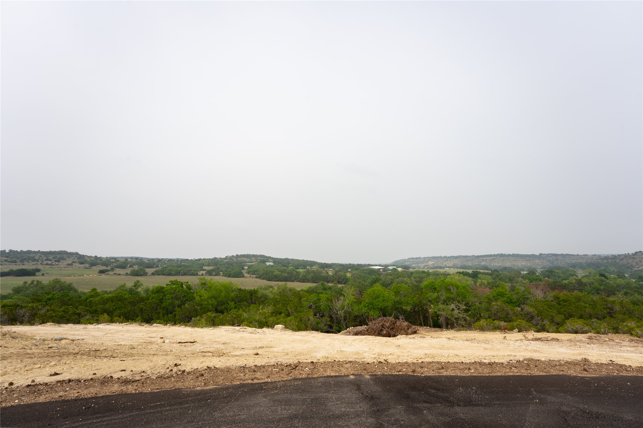 Lot 25 Ranch Road 165 Dripping Springs, TX 78620 - Photo 6 of 8 Expansive land parcel featuring a cleared building site, existing asphalt driveway, and distant green landscapes