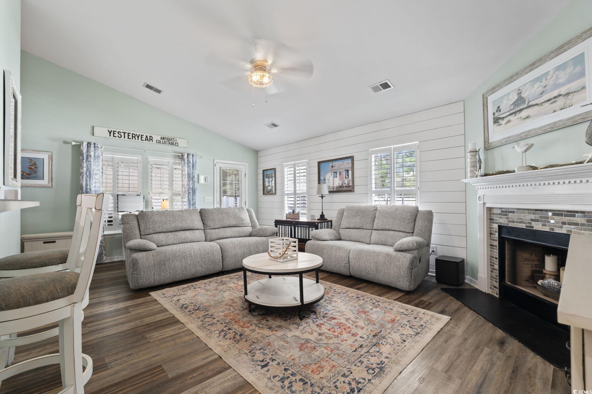 1604 Langley Drive Longs, SC 29568 - Photo 16 of 37 Living area with a fireplace with raised hearth, vaulted ceiling, dark wood-type flooring, wood walls, and ceiling fan