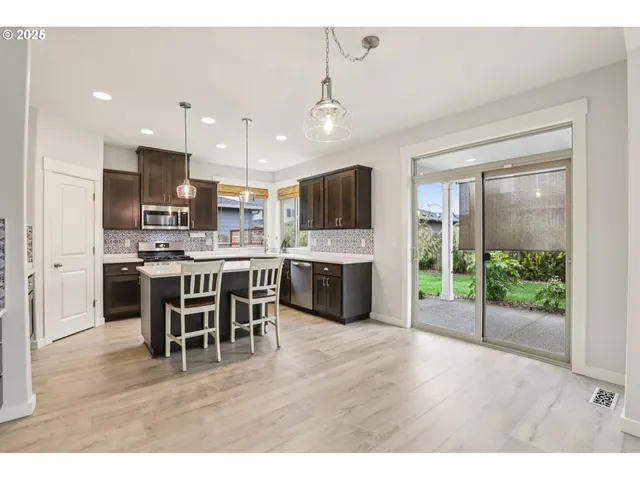 a open kitchen with stainless steel appliances granite countertop a stove top oven a sink dishwasher a dining table and chairs with wooden floor