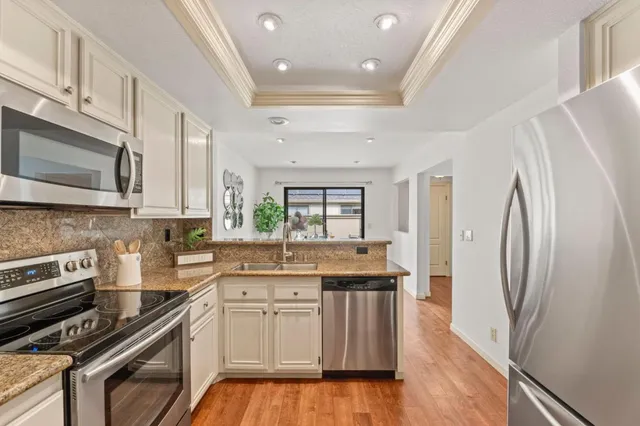 a kitchen with stainless steel appliances a stove a sink dishwasher a refrigerator white cabinets and wooden floor