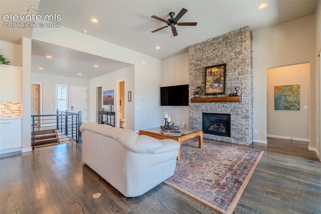 1061 Native Dancer Terrace Colorado Springs, CO 80921 - Photo 6 of 50 Living area featuring a stone-clad fireplace with a wood mantel, dark wood-finish flooring, recessed lighting, and a ceiling fan