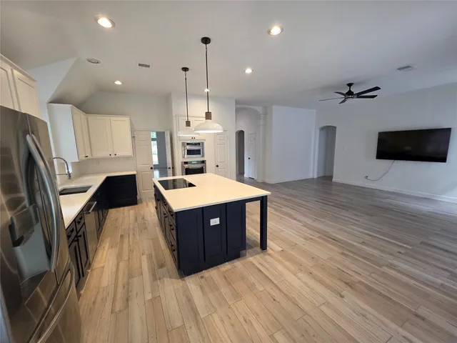 a large kitchen with stainless steel appliances a large counter top a stove a sink dishwasher and a refrigerator with wooden floor